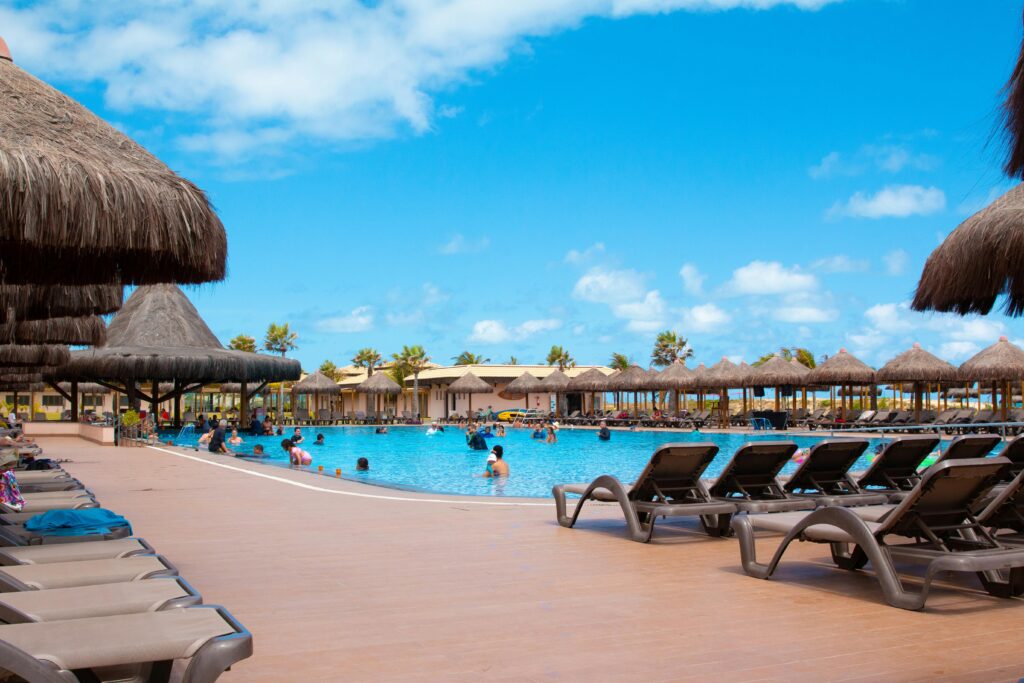 People enjoying a sunny day by the pool at a tropical resort with straw umbrellas.